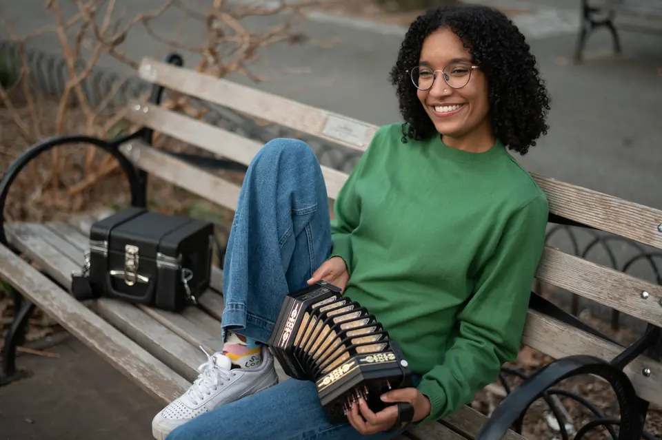 Zohra Coday smiling on a park bench, holding her concertina